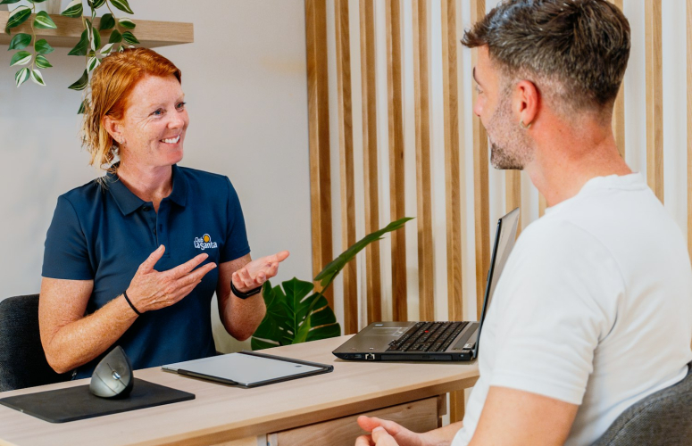 A women consulting with a person sat across from each other in a room with plants in the background.
