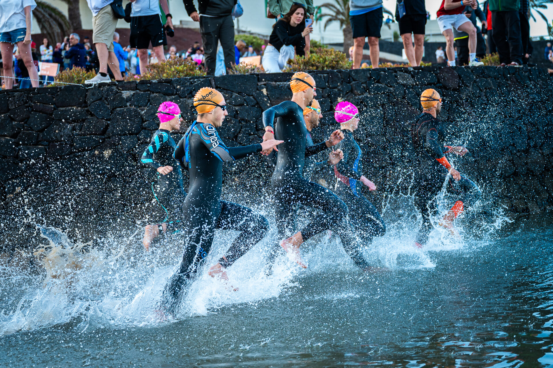 Group of people taking part in the Volcano Triathlon at Club La Santa Lanzarote, entering the water to start swimming.